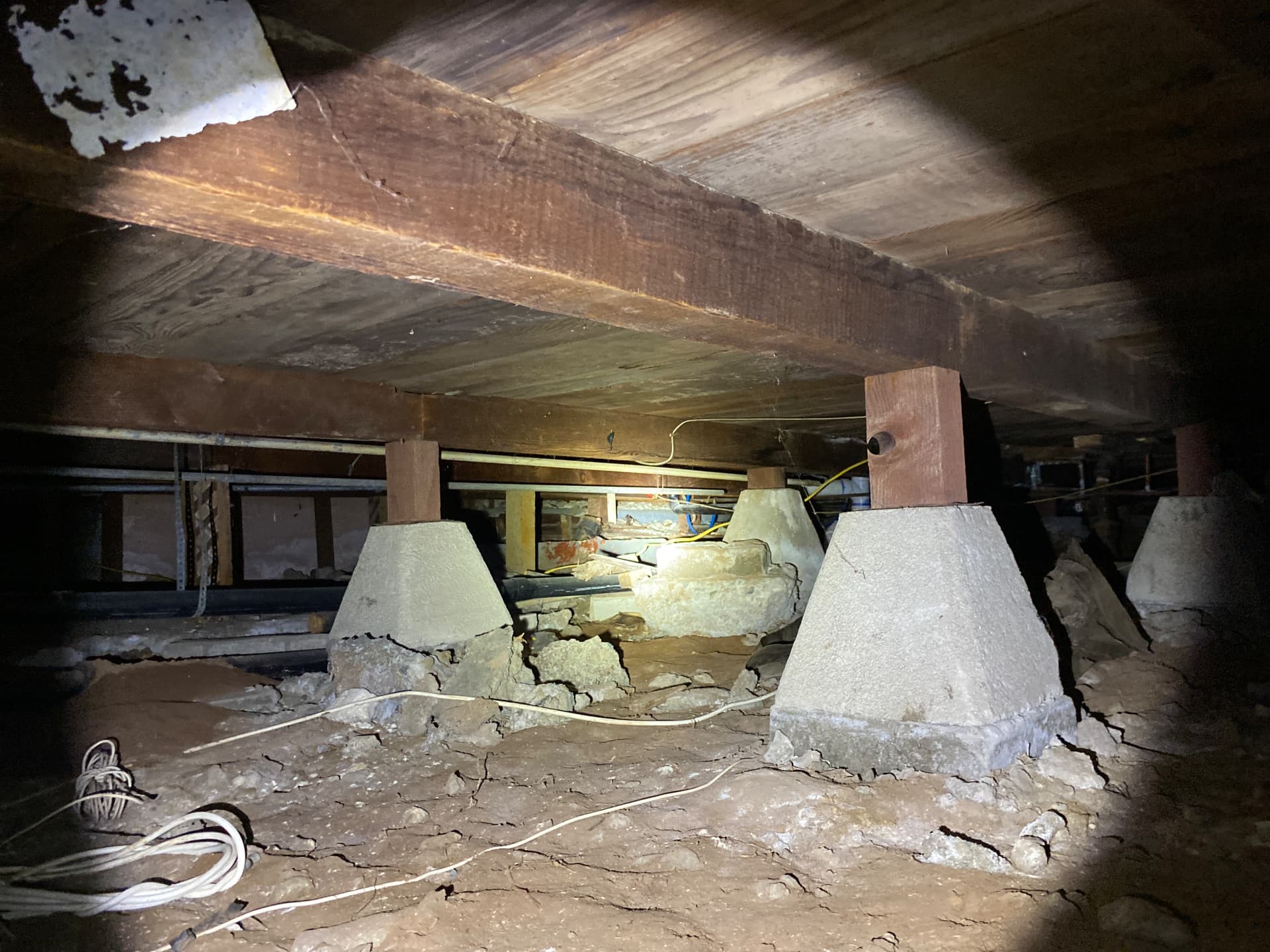 Crawlspace with wood posts on concrete piers, subfloor framing, and plumbing runs