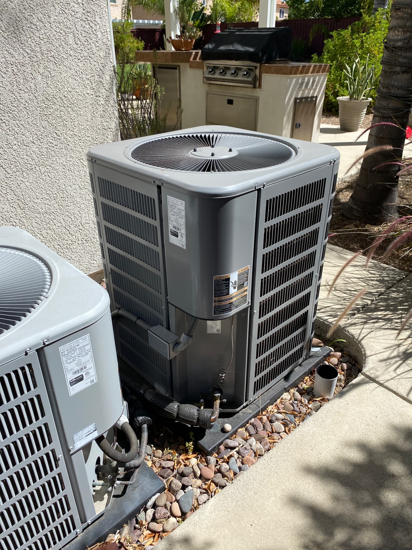 Two exterior air conditioning condenser units beside a stucco wall in a San Diego backyard